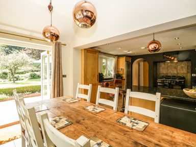 A dining area with a wooden table and white chairs next to a kitchen with wooden cabinets and black appliances at Valley House in Devizes