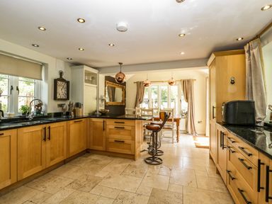 A kitchen with wooden cabinets black countertops a clock two copper pendant lights and a wooden dining table at Valley House in Devizes