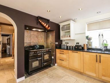 A kitchen with a black stove copper pans hanging wooden cabinets and a window with a sink at Valley House in Devizes