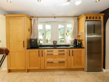 A kitchen with wooden cabinets a black countertop appliances and a window at Valley House in Devizes