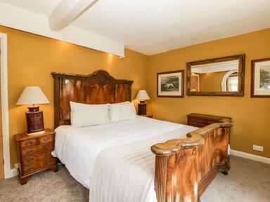 A bedroom with a wooden bed frame bedside tables with lamps mirror and framed pictures on mustard walls at Valley House in Devizes