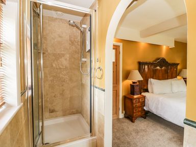 A shower area with tiled walls next to a bedroom with a wooden headboard bedside tables and lamps at Valley House in Devizes