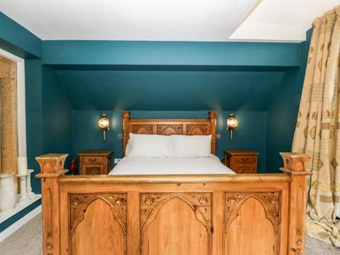 A bedroom with a wooden bed frame white bedding two wooden bedside tables wall lamps blue walls and patterned curtains at Valley House in Devizes