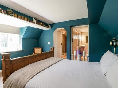 A bedroom with a wooden bed frame blue walls a chair near the window and an adjoining bathroom at Valley House in Devizes