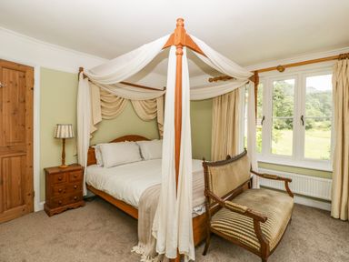 A bedroom with a four poster bed a bedside table with lamp and a wooden chair next to a window at Valley House in Devizes
