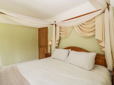 A bedroom with a wooden canopy bed with white bedding a wooden door and a bedside table with a lamp at Valley House in Devizes