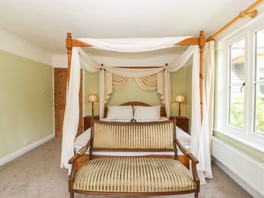 A bedroom with a four-poster bed draped with fabric two bedside tables with lamps and a wooden bench at the foot of the bed at Valley House in Devizes