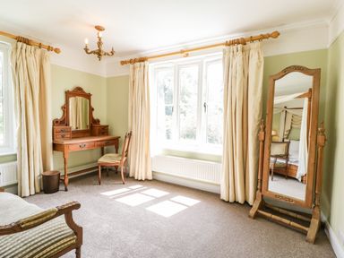 A bedroom with a dressing table chair full length mirror and windows with curtains at Valley House in Devizes