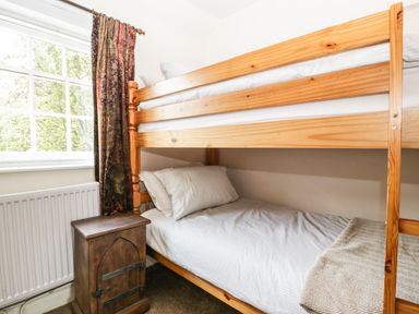 A bedroom with a wooden bunk bed next to a window with patterned curtains and a small wooden cabinet at Valley House in Devizes