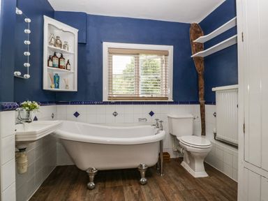 A bathroom with a clawfoot bathtub toilet sink and shelves with blue walls at Valley House in Devizes