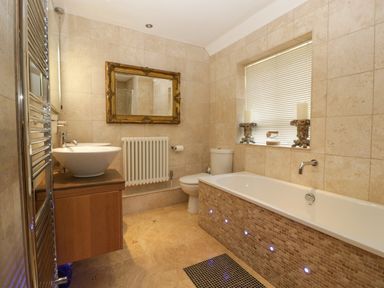 A bathroom with a bathtub a toilet two vessel sinks a mirror and a window with candles at Valley House in Devizes