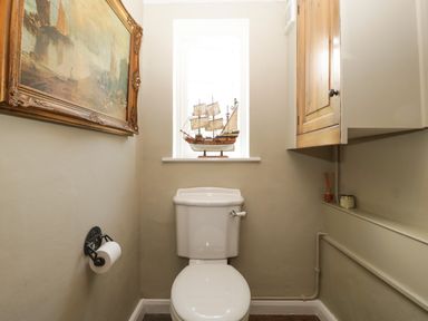 A small bathroom with a white toilet a model ship on the window ledge a framed painting on the wall and a wooden cabinet above a shelf at Valley House in Devizes