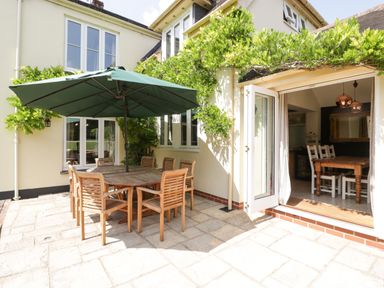 An outdoor patio with a wooden dining table and chairs under a green umbrella next to an open door to a dining room at Valley House in Devizes
