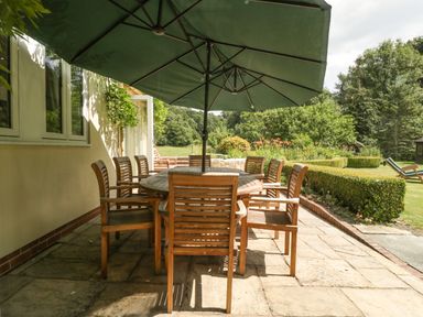 An outdoor patio with wooden table and chairs under a large green umbrella at Valley House in Devizes