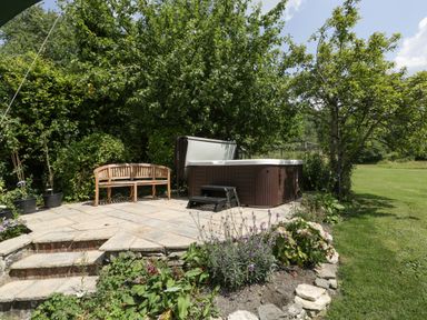 An outdoor patio area with a wooden bench and a hot tub near trees and a garden at Valley House in Devizes