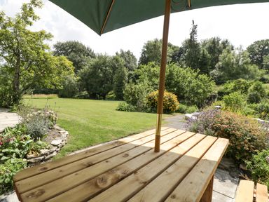 A wooden picnic table with an umbrella in a garden with trees and plants at Valley House in Devizes