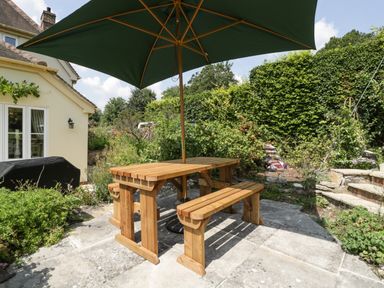 A wooden picnic table with benches and a green umbrella on a stone patio in a garden at Valley House in Devizes