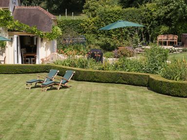 A garden with two lounge chairs on grass and a hedge near a house with an open door at Valley House in Devizes