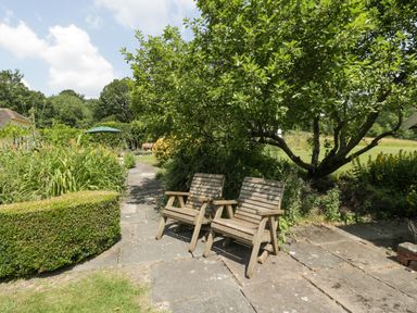 A garden with two wooden chairs on a stone patio under a tree at Valley House in Devizes