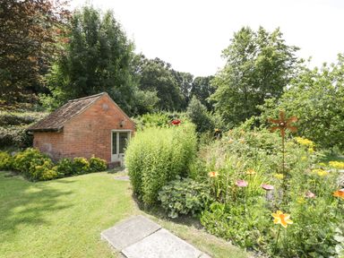 A garden with various plants and flowers next to a small brick building at Valley House in Devizes