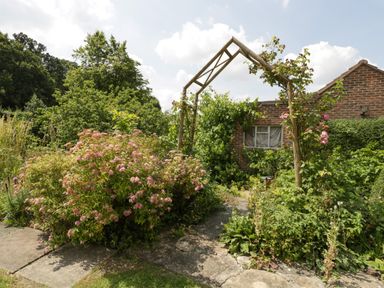 A garden with flowering plants a wooden arch and a brick building in the background at Valley House in Devizes