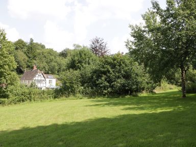A grassy field with trees and bushes and a house in the background at Valley House in Devizes