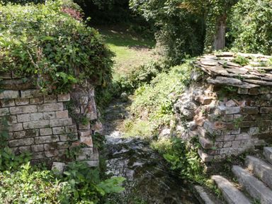 A small stream flowing between two old stone walls with greenery and plants surrounding it at Valley House in Devizes