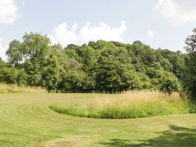 A grassy field with a curved mowed path and trees in the background at Valley House in Devizes