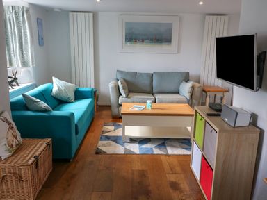A living room with two sofas a wooden coffee table a wall-mounted TV and a storage unit with colorful bins at Furneaux Hatch in Churchstow