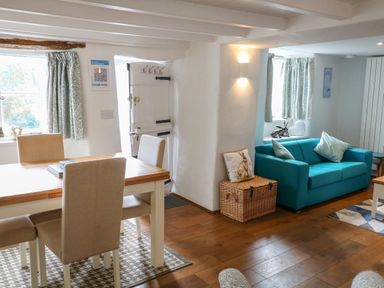 A dining area with a wooden table and beige chairs next to a blue sofa and wicker basket at Furneaux Hatch in Churchstow