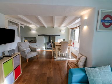 A living and dining area with a patterned armchair a wooden dining table with chairs a wood stove and a blue sofa at Furneaux Hatch in Churchstow