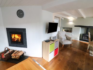 A living room with a fireplace wood storage clock armchair and a television on a cabinet at Furneaux Hatch in Churchstow