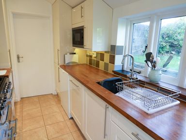 A kitchen with wooden countertops a sink with a drying rack utensils in a jug and a window at Furneaux Hatch in Churchstow
