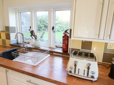 A kitchen countertop with a sink and dish rack a toaster and utensils in a jar near a window at Furneaux Hatch in Churchstow