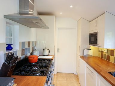A kitchen with a gas stove, knife block, kettle, microwave, and wooden countertops at Furneaux Hatch in Churchstow