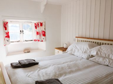 A bedroom with a bed and pillows next to a window with red and white curtains at Furneaux Hatch in Churchstow