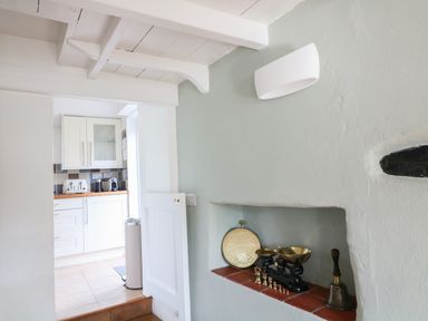 A wall with a built-in shelf holding a scale, small weights and a bell with a view into a kitchen at Furneaux Hatch in Churchstow