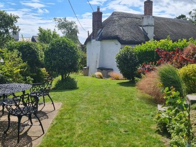 A garden with metal table and chairs and bushes near a thatched roof house at Furneaux Hatch in Churchstow