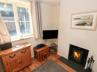 A room with a window and wooden cabinet a small television on nested tables and a wood burning stove with fireplace tools at Oysterbank Cottage in Llangwm Pembrokeshire