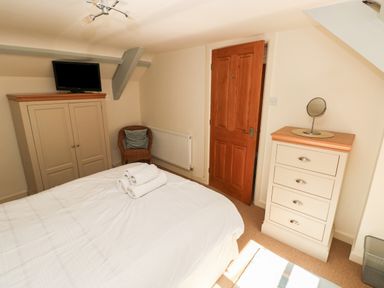 A bedroom with a bed with folded towels a wardrobe with a television a chair a chest of drawers with a mirror and a wooden door at Oysterbank Cottage in Llangwm Pembrokeshire