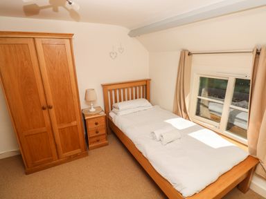 A bedroom with a single bed beside a window and wooden wardrobe and bedside table at Oysterbank Cottage in Llangwm Pembrokeshire
