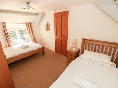 A bedroom with two single beds a bedside table with a lamp a wooden door and a window with curtains at Oysterbank Cottage in Llangwm Pembrokeshire