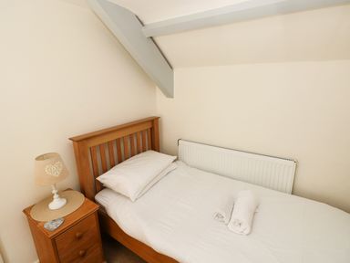 A small bedroom with a single wooden bed a bedside table with a lamp and two rolled towels on the bed at Oysterbank Cottage in Llangwm Pembrokeshire