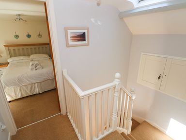 A staircase with white railing leading to a bedroom with a bed and rolled towels at Oysterbank Cottage in Llangwm Pembrokeshire