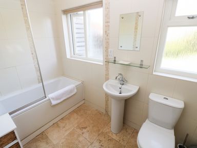 A bathroom with a bathtub a pedestal sink a toilet and two windows at Oysterbank Cottage in Llangwm Pembrokeshire
