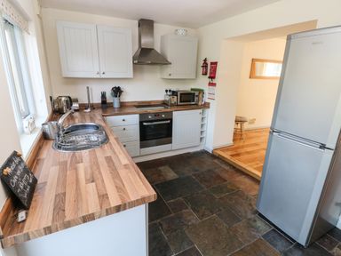 A kitchen with wooden countertops white cabinets stainless steel appliances and a tiled floor at Oysterbank Cottage in Llangwm Pembrokeshire