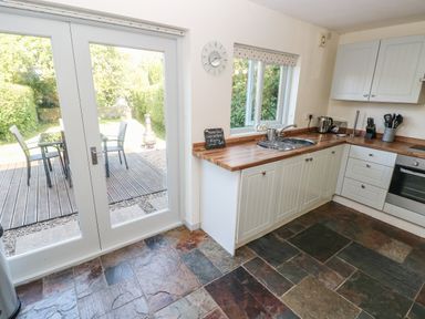 A kitchen with white cabinets wooden countertops and slate tile flooring with glass double doors leading to a garden at Oysterbank Cottage in Llangwm Pembrokeshire