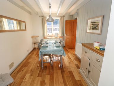 A dining room with a table set for four with bowls and glasses wooden chairs wooden floor sideboard and a window at Oysterbank Cottage in Llangwm Pembrokeshire