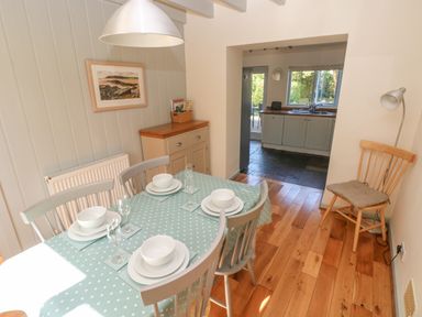 A dining area with a table set for four and a kitchen visible through an open doorway at Oysterbank Cottage in Llangwm Pembrokeshire
