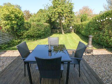An outdoor patio with a glass table and four chairs overlooking a lawn with a tree and surrounded by hedges at Oysterbank Cottage in Llangwm Pembrokeshire